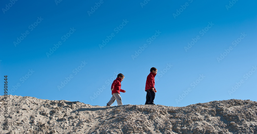 Two brothers walking on a sand hill.