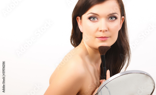 Beautiful woman applies make-up, holds mirror near face photo