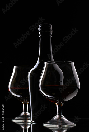 Glasses of brandy and bottle on black background