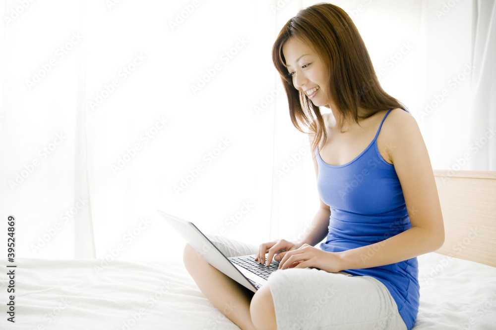 Naklejka premium ベッドの上で胡座をかきノートパソコンを使っている女性