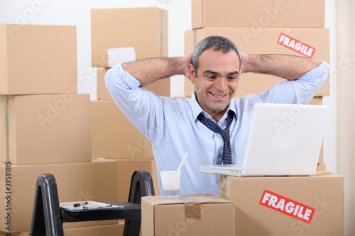 Man surrounded by cardboard boxes using his laptop © auremar