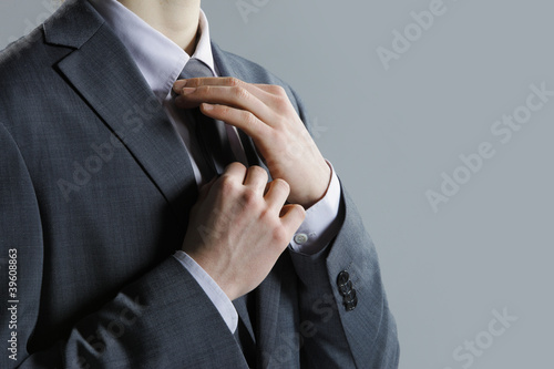 A businessman in a  grey suit checking his necktie photo