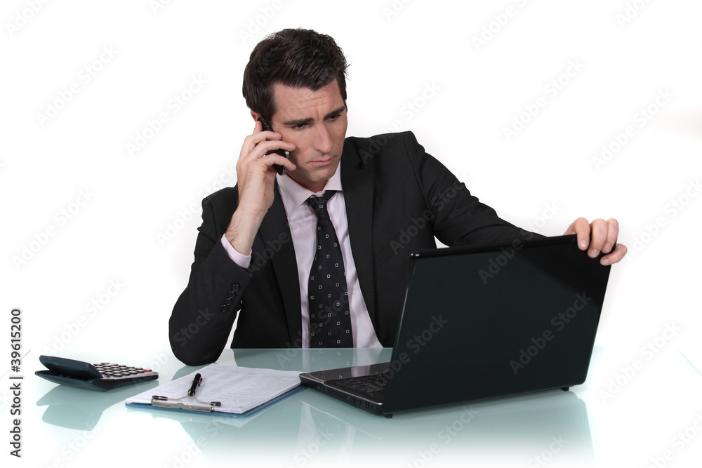 Businessman making call whilst reading from computer screen Businessman making call whilst reading from computer screen