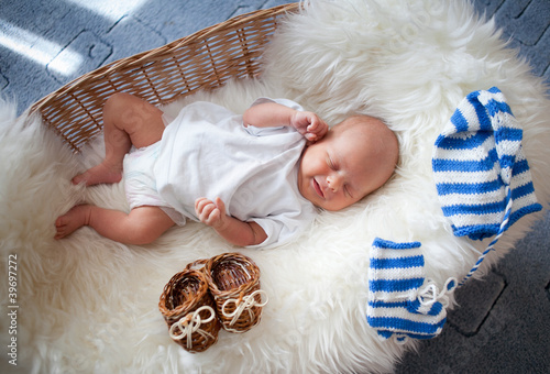 Obraz na plátně Sleeping newborn baby in wicker basket lying on sheepskin