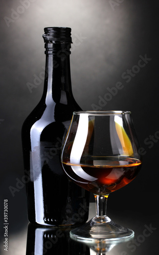 Glass of brandy and bottle on gray background
