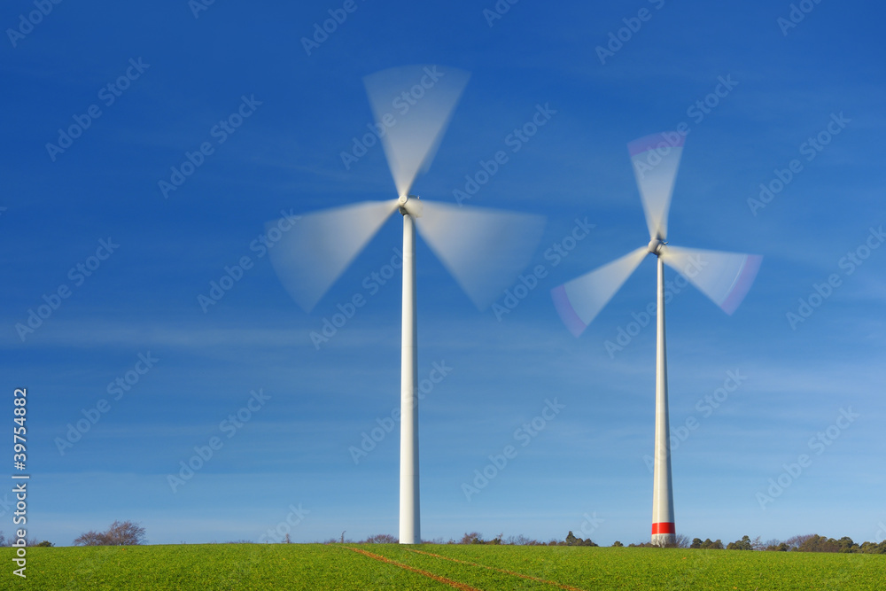 Fototapeta premium Two wind turbines in movement on a green field