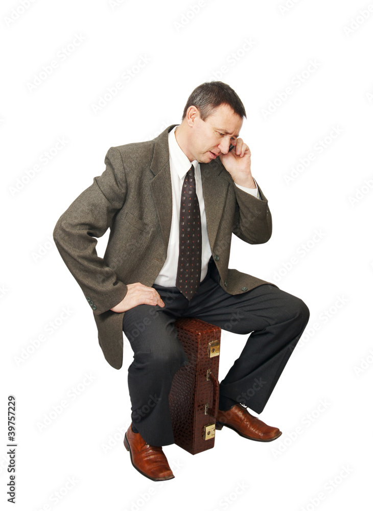 Businessman sits on suitcase and talks by phone Businessman sits on suitcase and talks by phone