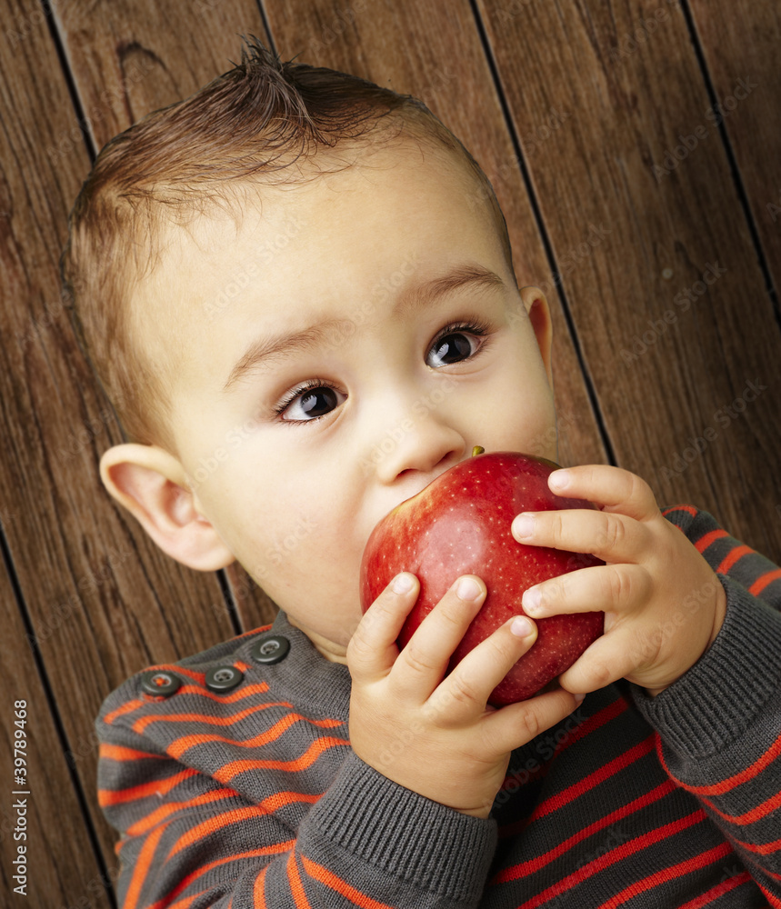 portrait of a handsome kid sucking a red apple against a wooden portrait of a handsome kid sucking a red apple against a wooden