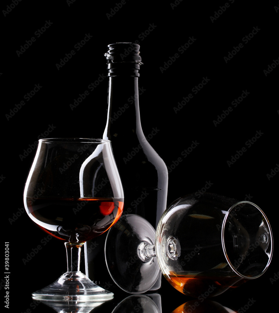 Glasses of brandy and bottle on black background