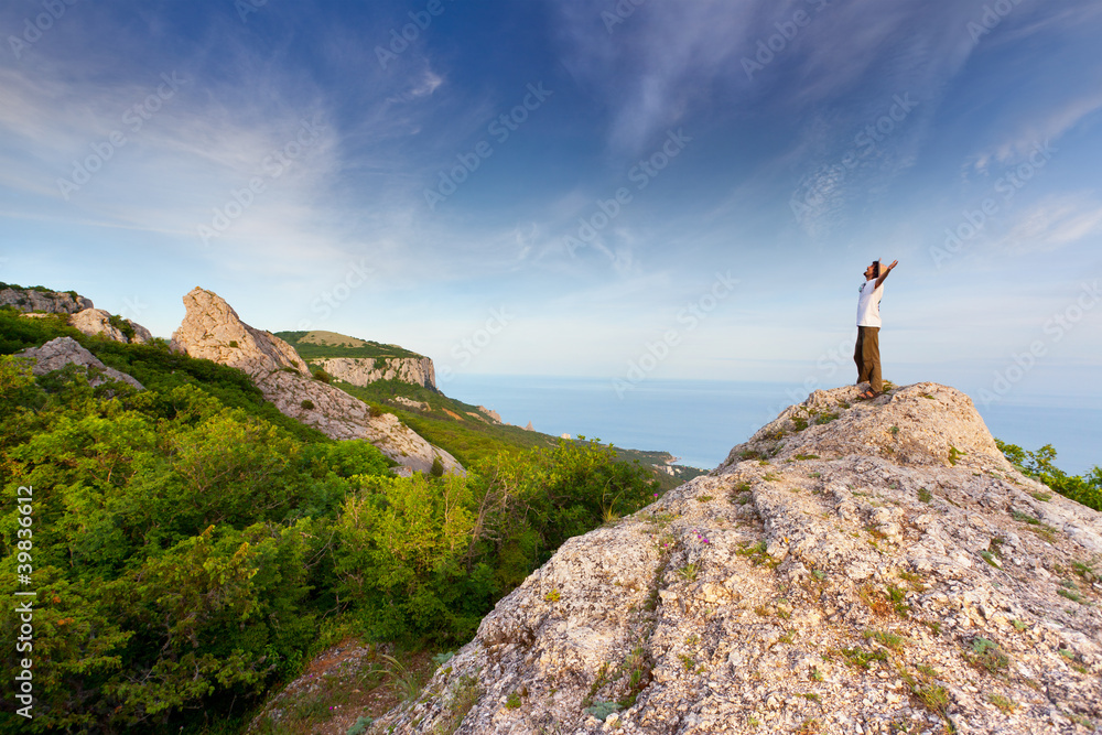 Fototapeta premium hiker at the top of a rock with his hands up enjoy sunny day