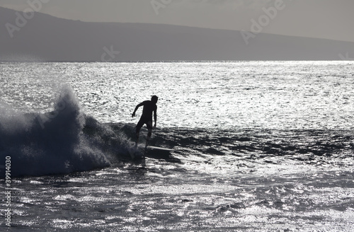 surfer silhoutted against the silver waves on maui coast