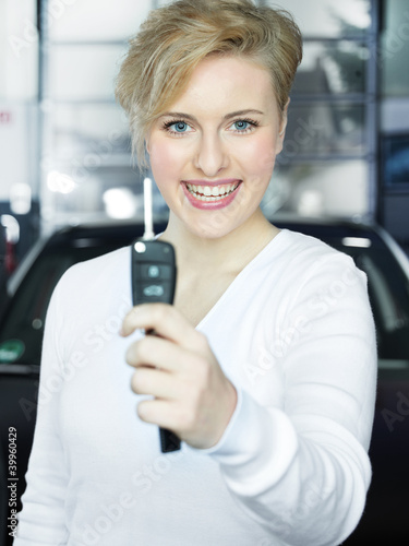 Pretty blonde woman proudly presents the key of her new car