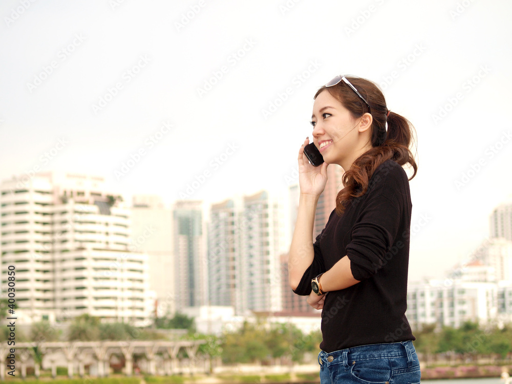 Young pretty Asian calling by phone with building background