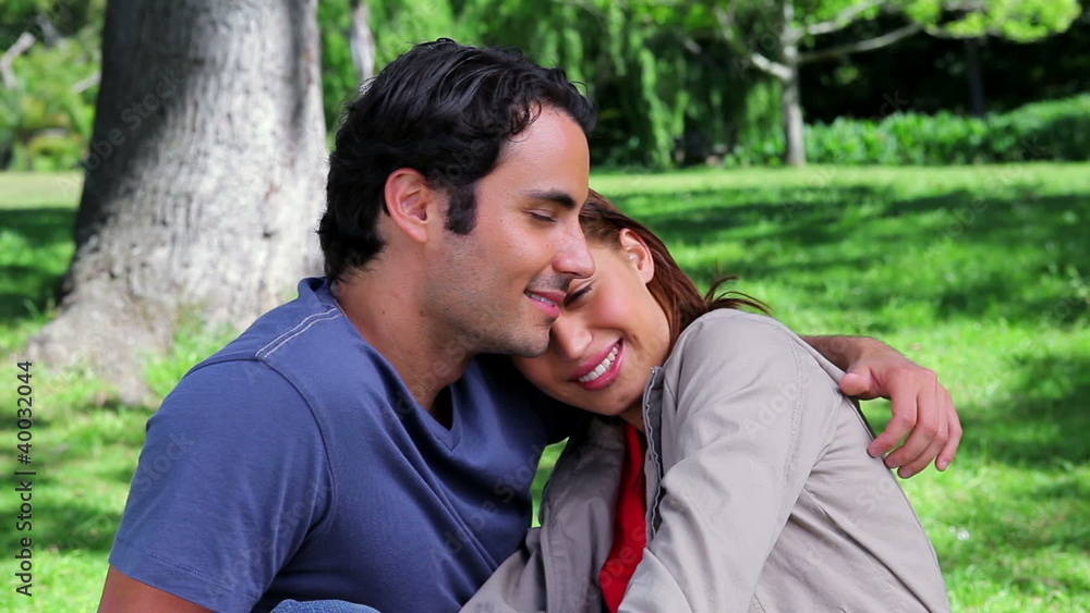 Smiling couple hugging each other while sitting on the grass Smiling couple hugging each other while sitting on the grass