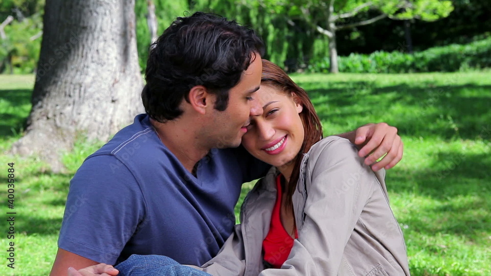 Happy couple embracing each other while sitting on the grass Happy couple embracing each other while sitting on the grass