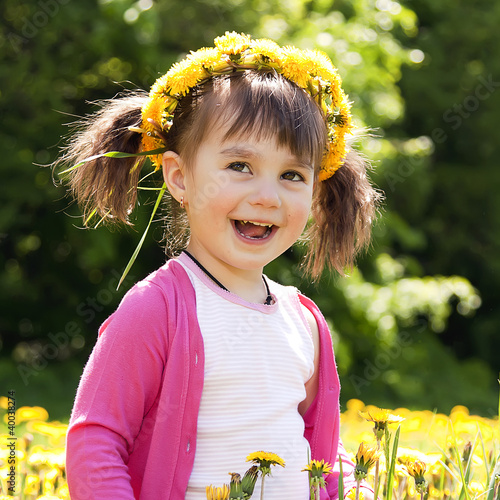 A smiling girl sitting on the dandelion field with the dandelion