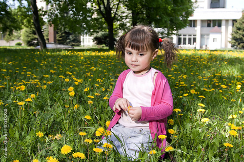 A smiling girl sitting on the dandelion field wearing a pink sh