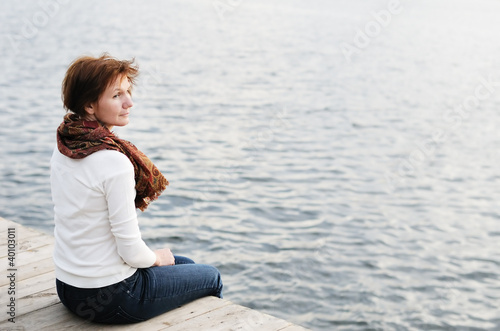 Middle age woman sitting on wood boards by the water