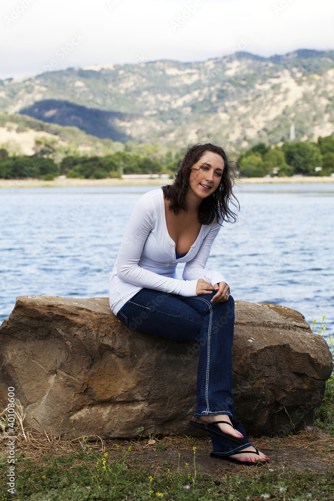 Young Caucasian Woman Sitting On Rock Lakeside