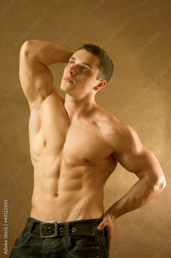 Fototapeta premium A muscular man posing in studio on brown background
