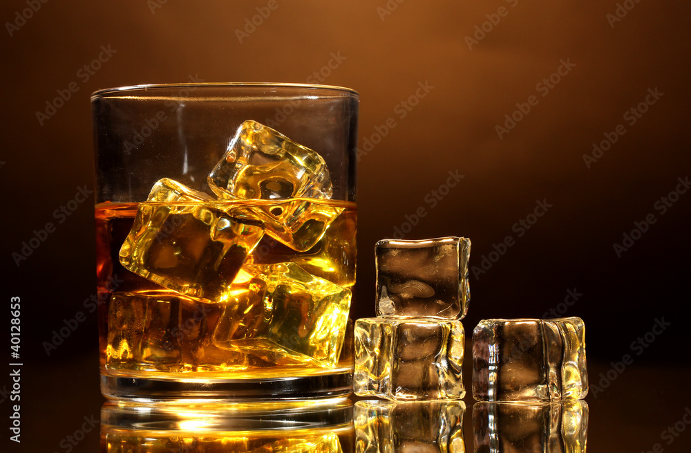 glass of whiskey and ice on brown background glass of whiskey and ice on brown background