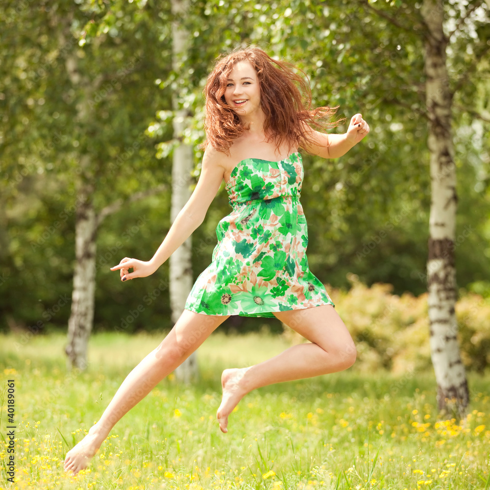 Young redhead woman jumping in the park with flowers Young redhead woman jumping in the park with flowers