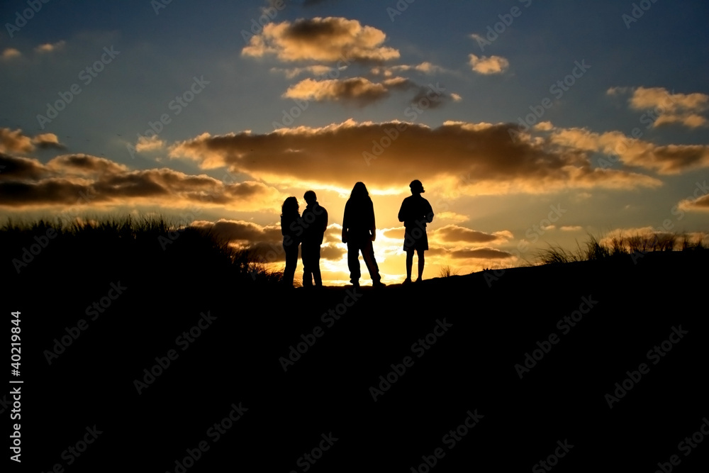 silhouette of friends standing on dune in sunset