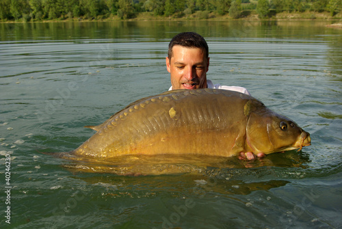 Fototapeta Naklejka Na Ścianę i Meble -  Happy  fisherman holding a giant mirror carp