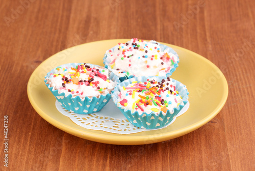 Creamy cupcakes on saucer on wooden background