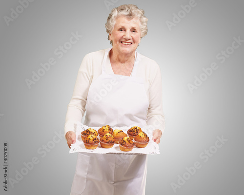 portrait of cook senior woman holding a chocolate muffins tray o
