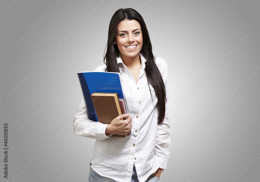 young student holding books and smiling against a grey backgroun young student holding books and smiling against a grey backgroun