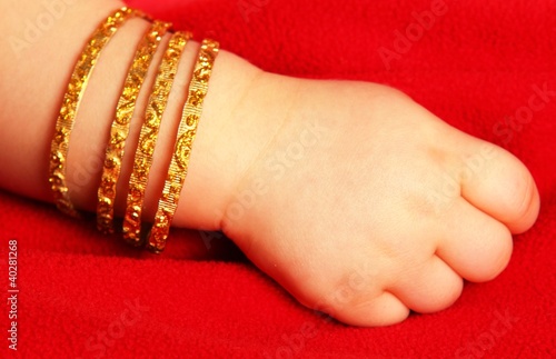 Baby hand, with golden bracelets, isolated towards dark red
