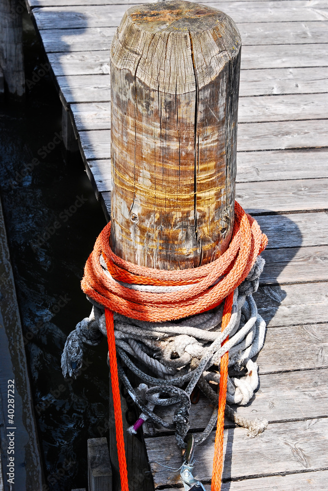 Fototapeta premium an orange rope wrapped around a timber stump at a shipping pier