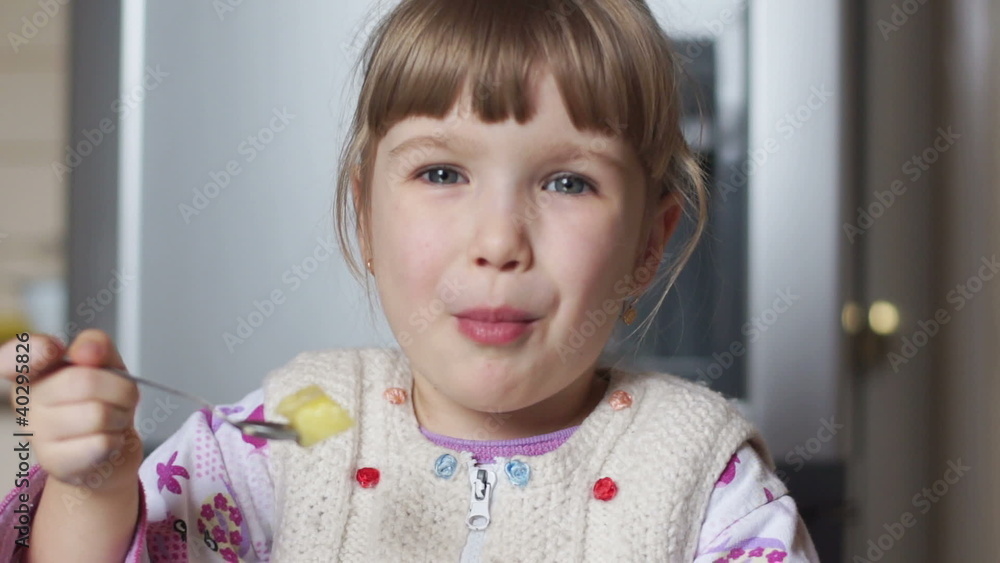 Baby girl eating potatoes in the kitchen. She smiles Baby girl eating potatoes in the kitchen. She smiles
