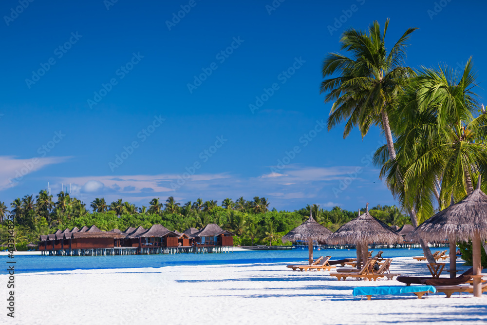 Palm trees over sandy tropical beach with villas over water