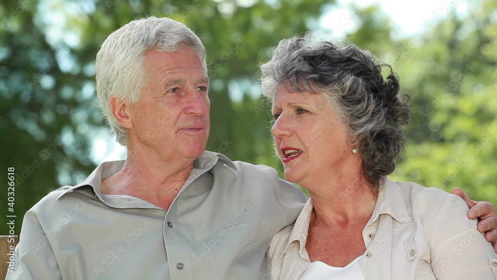 Happy mature couple talking while sitting on a wooden bench Happy mature couple talking while sitting on a wooden bench