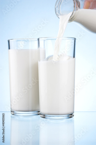 Pouring milk from a bottle into the two glasses on a blue backgr