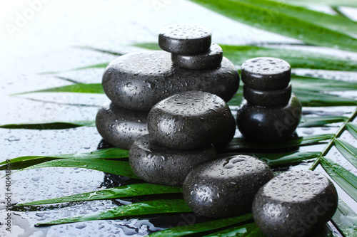 Spa stones with drops on green palm leaf on grey background