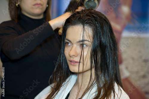 Pretty lady sitting while hairdresser dries her hair