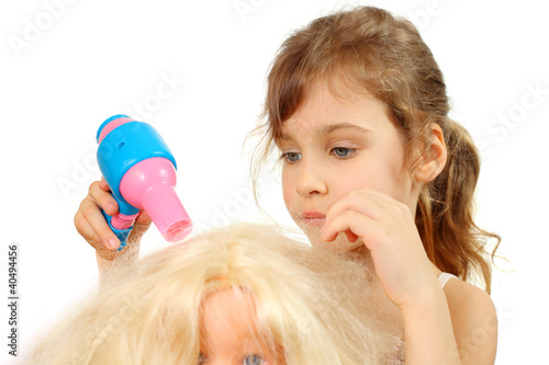 Little girl dries doll hair by bright toy hair dryer isolated photo