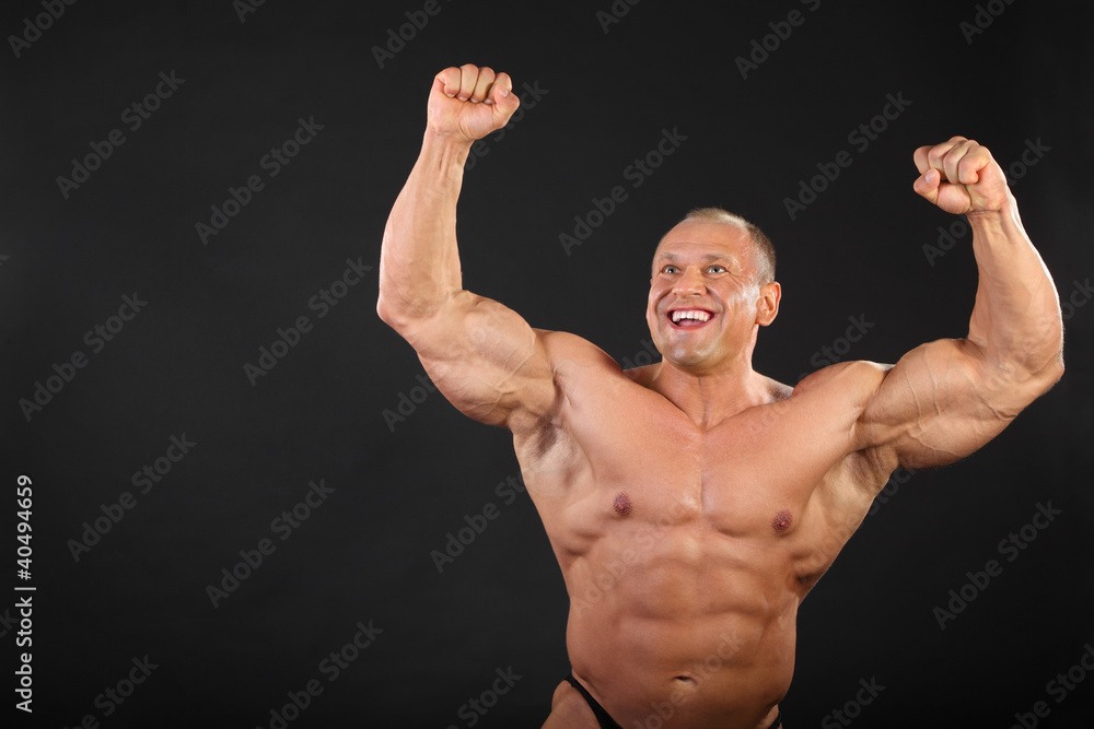 Undressed tanned happy bodybuilder raises his fists up