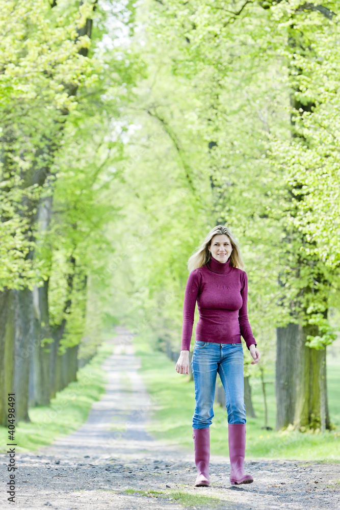 woman wearing rubber boots walking in spring alley woman wearing rubber boots walking in spring alley