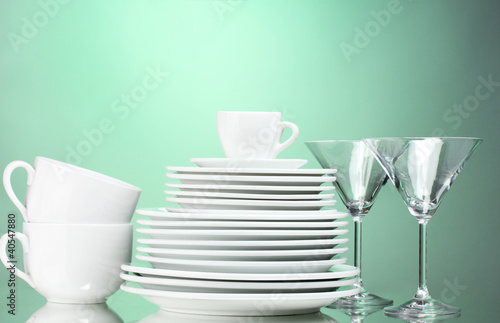 Clean plates, cups and glasses on green background