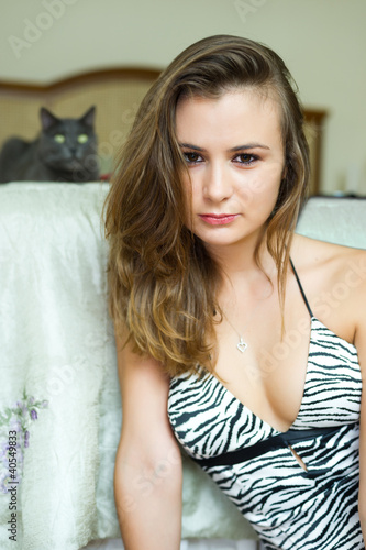 Young woman in leopard pattern top sitting in bedroom with a cat
