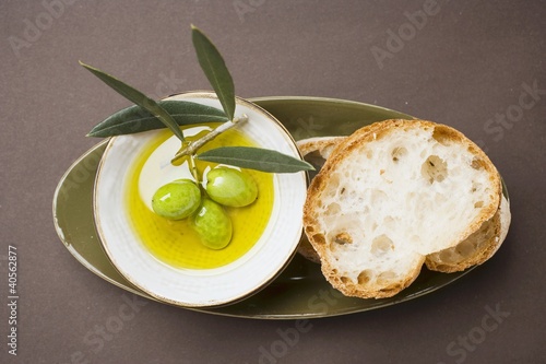 Green olives on twig in bowl of olive oil, white bread