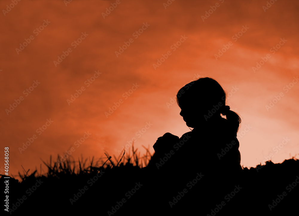 Alone little girl sitting on meadow in sunset - silhouette