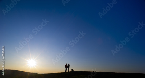 Family is hiking with a dog on a mountain in sunshine