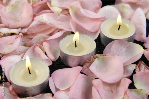 Three burning candles surrounded by rose petals