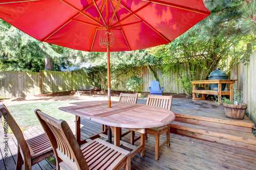 Back yard large deck with red umbrella and chairs.