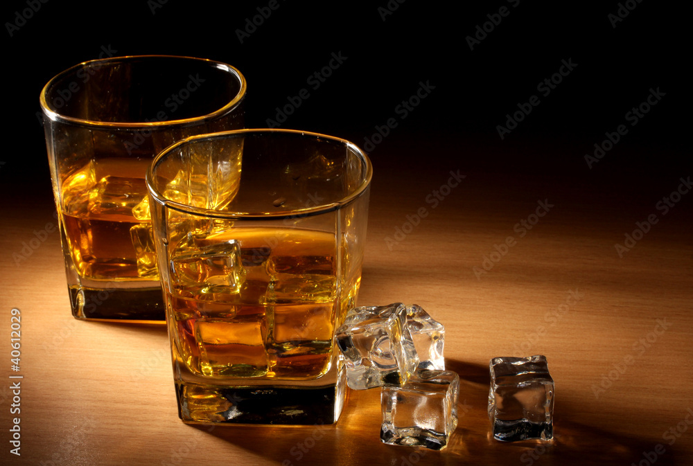 two glasses of scotch whiskey and ice on wooden table